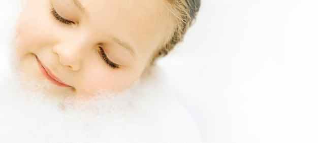 Cute little kid girl taking bath with white foam soap bubbles with copy space for text