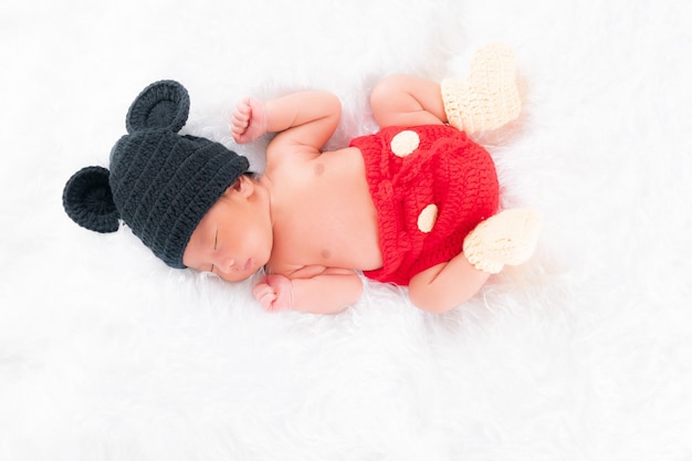 Cute little newborn boy wearing a black hat, cute red pants is sleeping in a white bed. Concept portrait studio fashion newborn.