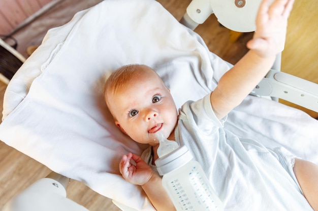 Cute little newborn girl drinking milk from bottle and looking at camera on white background infant ...