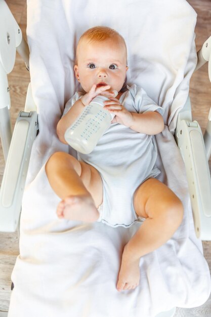 Cute little newborn girl drinking milk from bottle and looking at camera on white background infant ...