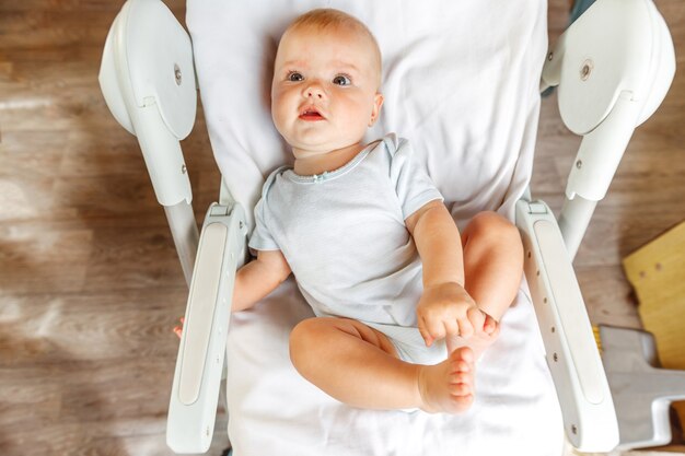 Cute little newborn girl with smiling face looking at camera on white background. Infant baby resting playing lying down on feeding chair at home. Motherhood happy child concept.