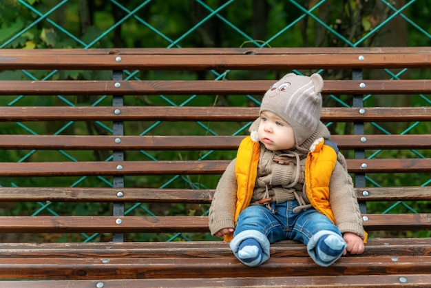 Cute little one-year-old baby on a park bench looks into the side. Attractive boy portrait in the park. Copy space for text.