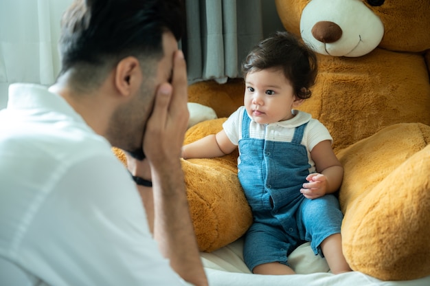 Cute little playful girl child learning to walk and stand by taking support of couch at home while looking away mischievously