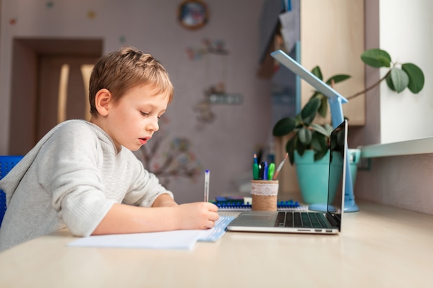 Cute little schoolboy studying at home doing school homework. Training books and notebook on the table. Distance learning online education