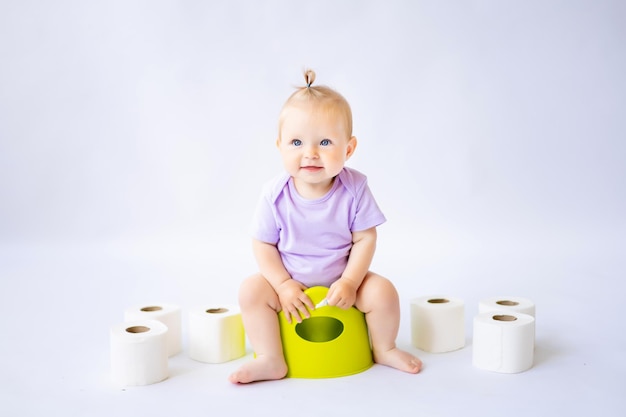 A cute little smiling girl is sitting on a pot with toilet paper rolls isolated on white background