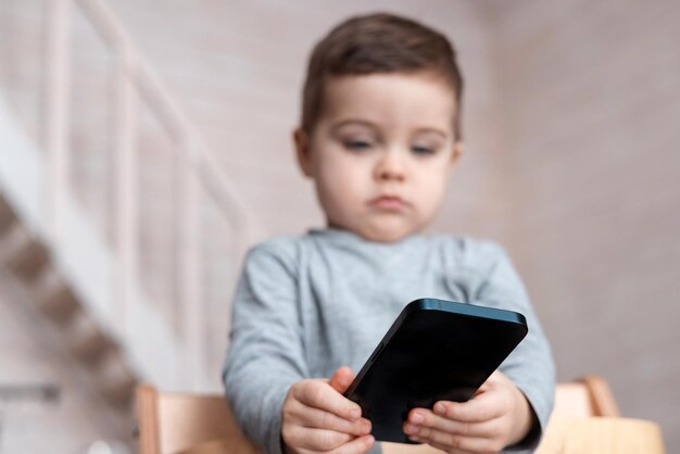 Photo cute little toddler boy playing with smartphone healthy baby touching mobile phone with fingers look...