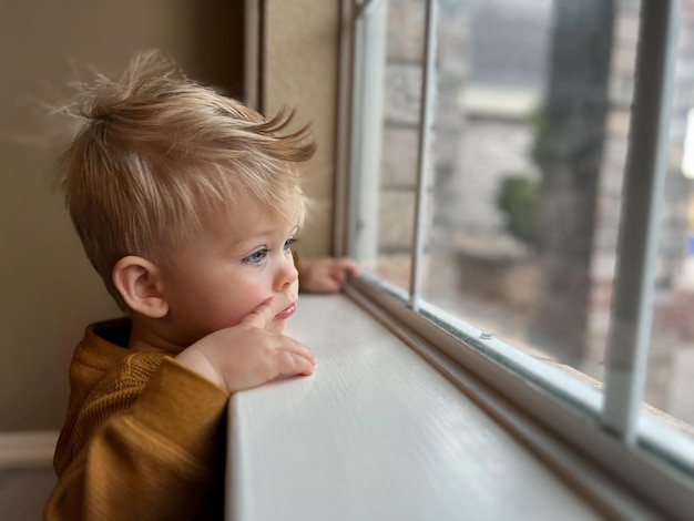 Cute little toddler looking at the window at home, close up portrait