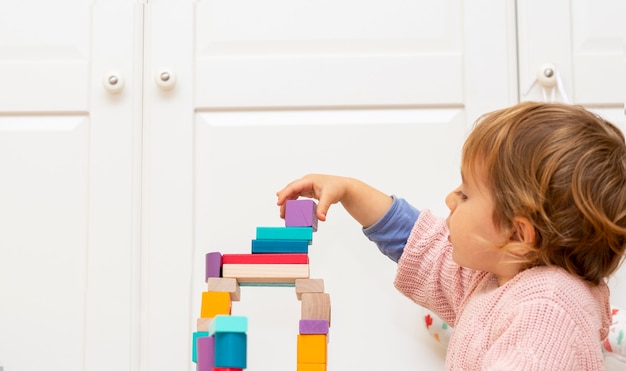 Cute and lovely child girl at home, playing with wooden building blocks toys.