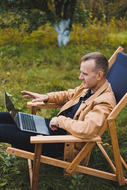 Cute man in a shirt sitting in a chair outdoors in the garden and working on a laptop remote work female freelancer