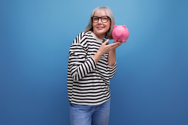 Cute middleaged woman holding a piggy bank with money on a bright background with copy space