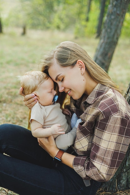 A cute mother is sitting in the park on the grass with a small child in her arms A walk with a small child in nature