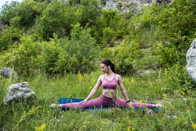 Cute nice brunette in a raspberry top and leggings near the rock stretches her body for the health of the body The concept of stretching in nature