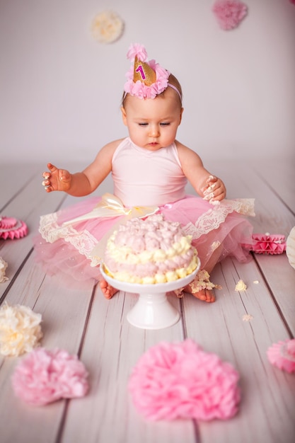 Cute oneyearold little baby girl with her first birthday cake trying sugar and celebrating birthday