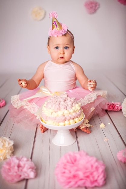 Cute oneyearold little girl with her first birthday cake trying sugar and celebrating birthday