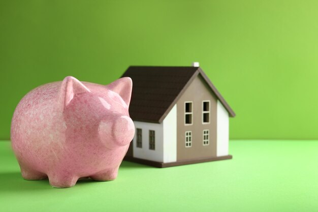 Cute piggy bank with house model on color background