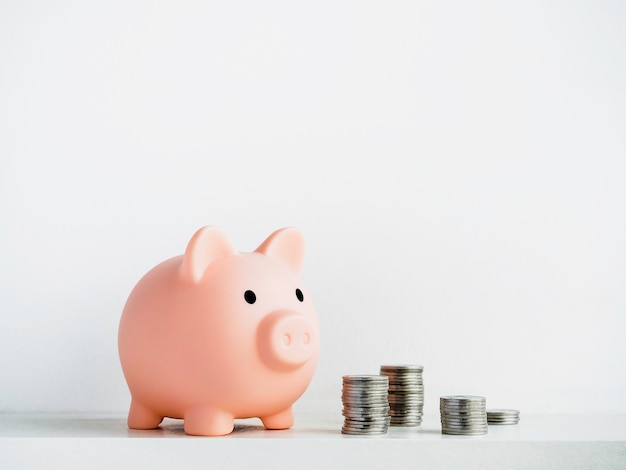 Cute piggy bank with piles of coins isolated on white surface