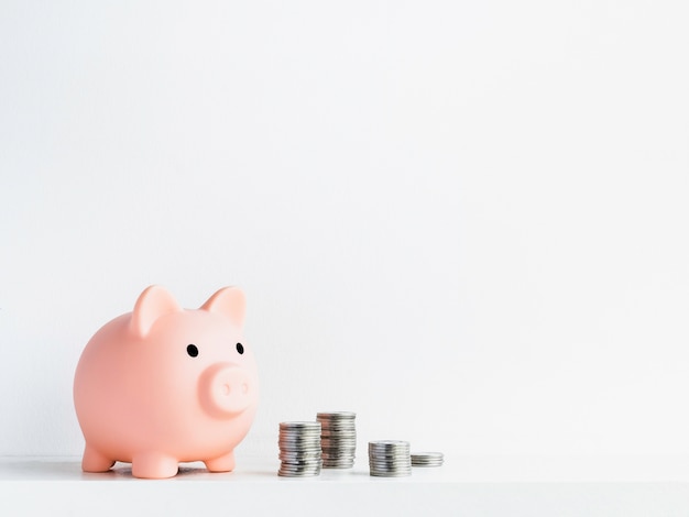 Cute piggy bank with piles of coins isolated on white surface