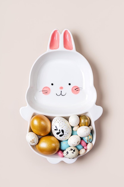 Cute plate in the shape of a bunny with Easter eggs and candy on beige background Happy Easter concept