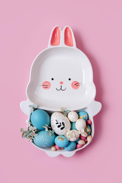 Cute plate in the shape of a bunny with Easter eggs and candy on pink background Happy Easter concept