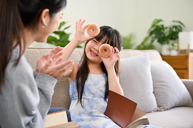 A cute and playful young Asian girl holding doughnuts playing peekaboo with her mom