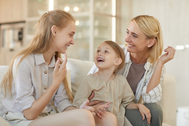 Cute portrait of carefree young mother talking to two daughters and smiling cheerfully while enjoying time together at home