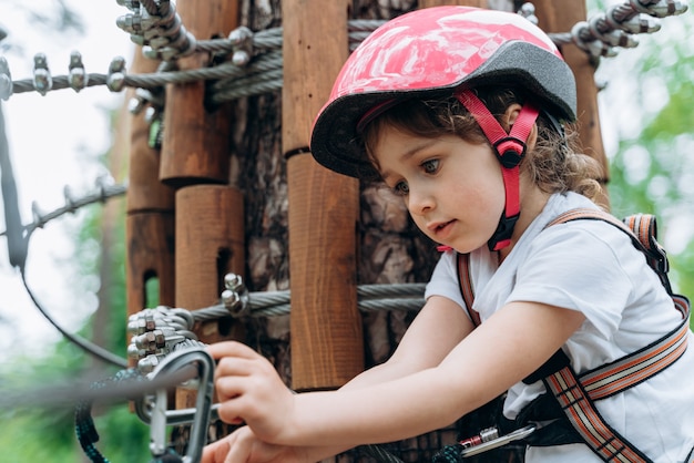 Cute, positive girl in a protective helmet carefully hooks the carbines on the rope. The little girl is actively spending time