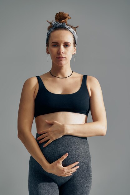 Cute pregnant belly isolated on gray Side view of young pregnant woman embracing her abdomen with hands Big belly on the third trimester of pregnancy closeup Concept of pregnant life