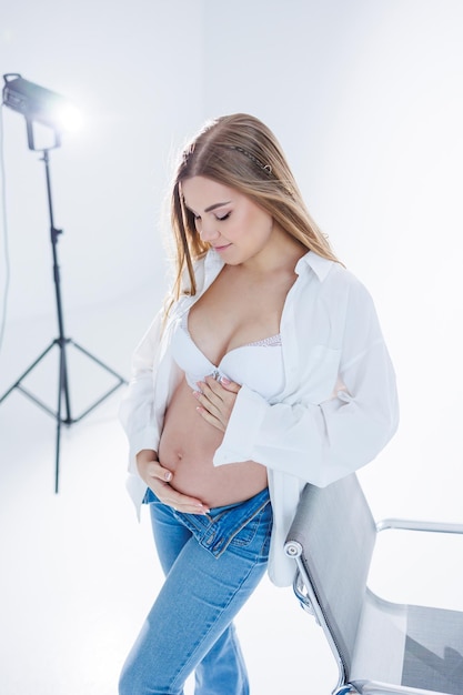 Cute pregnant woman in bra and white shirt on white background Happy pregnant woman stroking her belly