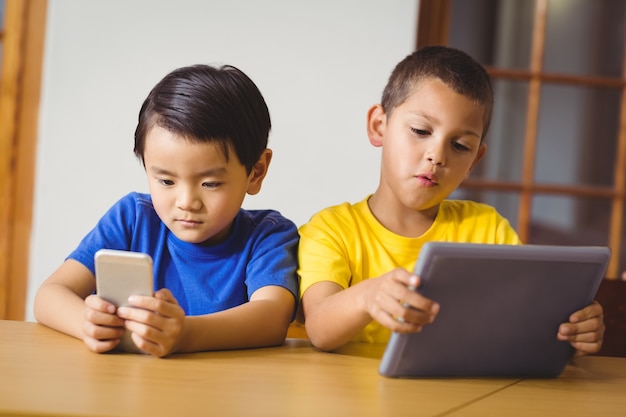 Cute pupils in class using phone and tablet 