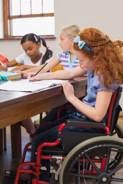 Cute pupils writing at desk in classroom at the elementary school