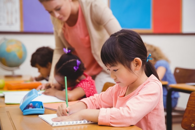 Cute pupils writing at desk in classroom