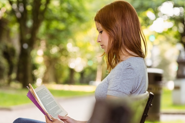 Cute redhead relaxing on bench and reading book