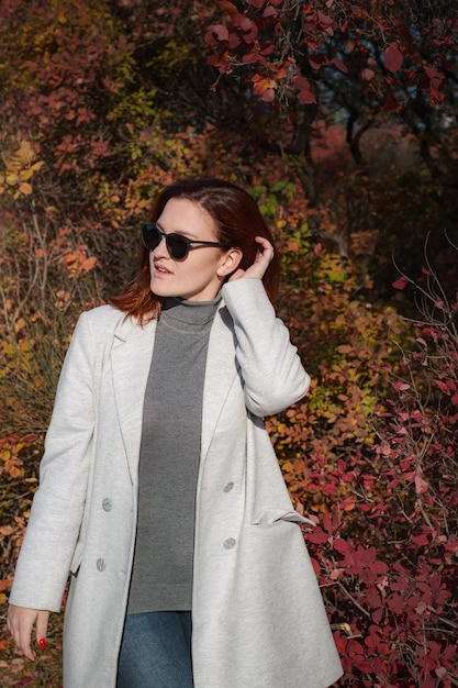 A cute redheaded woman in good spirits poses on an autumn day