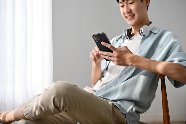 Cute and relaxed young Asian man sits on chair chatting with his friends on the phone