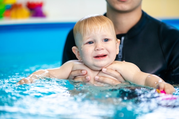 Cute sad baby boy learning to swim in special pool for little children