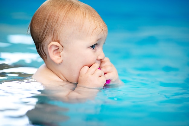 Cute sad baby boy learning to swim in special pool for little children.