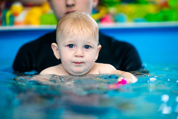 cute sad baby boy learning to swim in special pool for little children