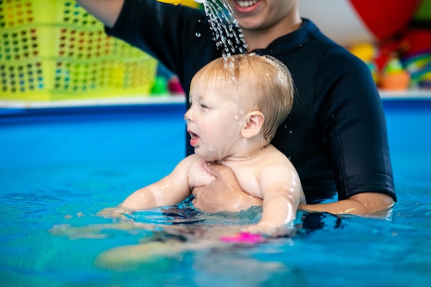 cute sad baby boy learning to swim in special pool for little children