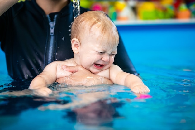 cute sad baby boy learning to swim in special pool for little children