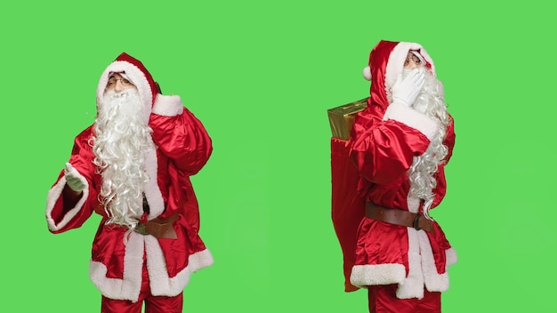 Cute santa claus sending air kisses, acting sweet with flirty gesture in greenscreen studio. Romantic man acting like saint nick on camera, carry bag with presents during christmas eve holiday.