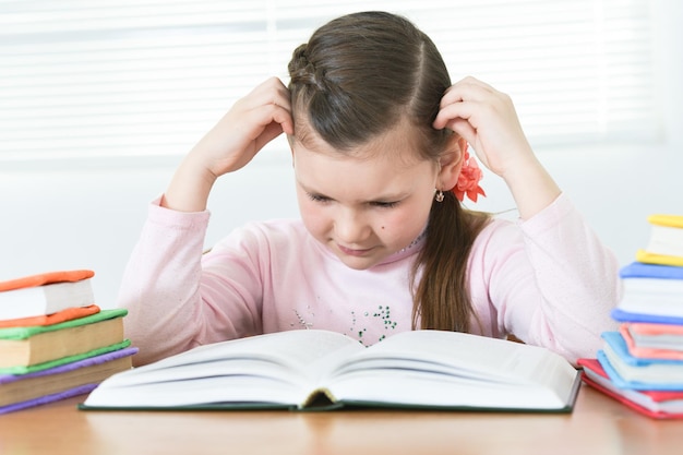 Cute schoolgirl sitting at table and doing homework at home