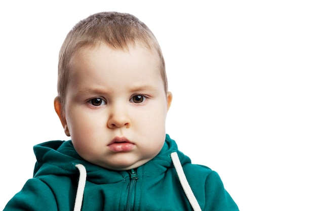 A cute serious boy with chubby cheeks A disgruntled kid in a green sweater is looking attentively Isolated on white background Closeup