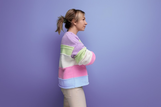 Cute shy blond young woman standing in profile on purple background with copy space