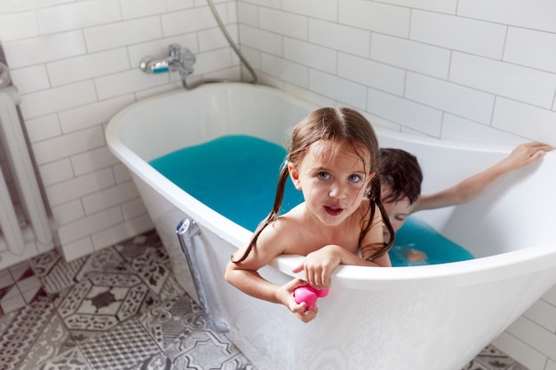 Cute siblings bathing in bathtub together in blue water