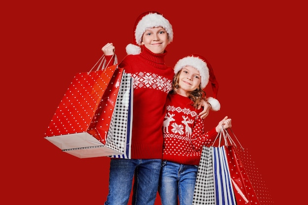 Cute siblings in red sweater holding shopping bags