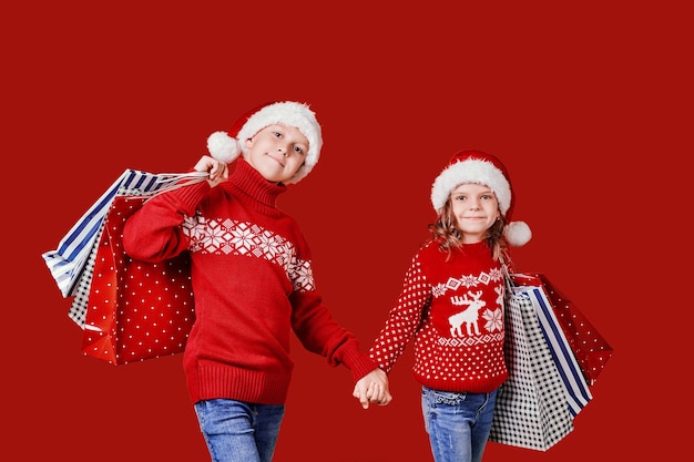 Cute siblings in red sweater holding shopping bags