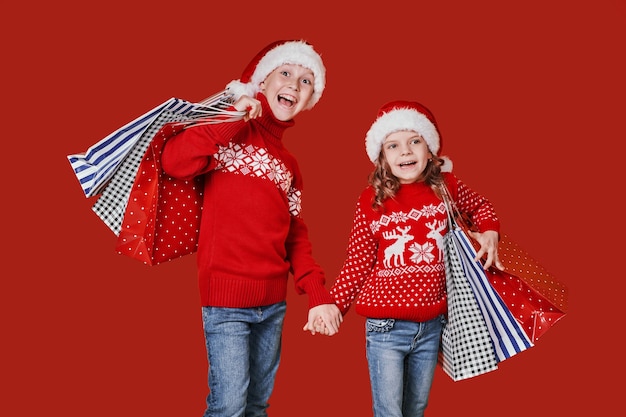 Cute siblings in red sweater holding shopping bags