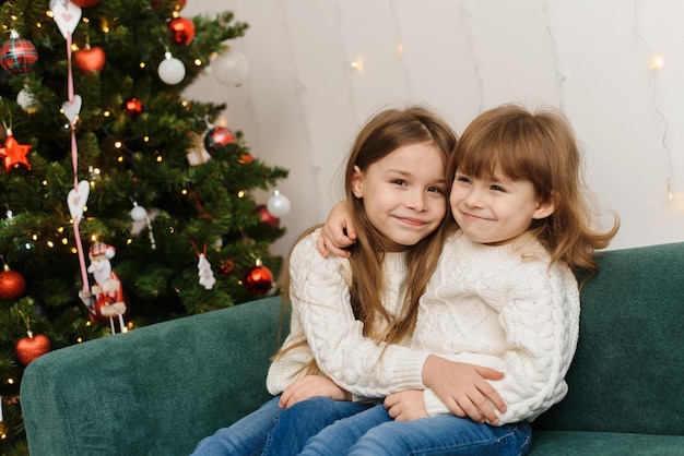 Cute sisters are sitting in a Christmas interior in white sweaters Christmas and New Year