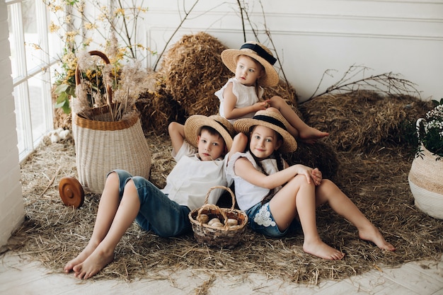 Cute sisters and brother in hay hats resting on hay