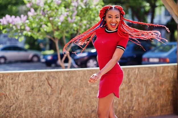 Cute and slim african american girl in red dress with dreadlocks in motion having fun on street Stylish black model